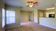 This single-floor residence offers a thoughtfully designed layout with a welcoming and functional aesthetic. The main living area is generously sized, featuring plush wall-to-wall carpeting that adds warmth underfoot. Crown molding lines the ceilings, lending a refined architectural touch, while a ceiling fan with integrated lighting provides both comfort and illumination. A two-tone wall treatment, with a chair rail dividing the upper and lower sections, adds classic detailing to the interior.

Natural light filters in through a window fitted with horizontal blinds, brightening the space. Recessed track lighting provides additional overhead illumination, ideal for accent or task lighting. A half-wall partition with a granite or stone countertop edge hints at a connected kitchen or breakfast bar area, offering a sense of openness between living and culinary spaces.

Toward the rear of the main room, a doorway leads to what appears to be a private bedroom with an en-suite bathroom and walk-in closet visible beyond. Clean white trim and neutral green-toned walls create a calm, cohesive palette throughout, making this a move-in-ready space well-suited for everyday living.