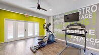 This single-level fitness center is thoughtfully designed to support a full range of workout activities. The main cardio area features hardwood-style flooring and is anchored by an eye-catching typographic wall mural showcasing motivational words in bold green and white lettering. A ceiling-mounted fan and recessed lighting keep the space comfortable, while a wall-mounted flat-screen TV adds entertainment during workouts. French doors along one wall flood the room with natural light and provide access to an outdoor area. Cardio equipment, including an elliptical trainer and treadmill, is well-positioned for use.

An adjacent strength training zone offers rubber flooring for safety and comfort, floor-to-ceiling mirrors that visually expand the space, and a dedicated storage rack stocked with stability balls and medicine balls in various sizes. An adjustable workout bench sits at the center of this area, ready for a variety of exercises. Motivational wall graphics continue the energetic aesthetic throughout.

A practical mudroom connects to the fitness space, featuring built-in cabinetry with open shelving, wall hooks, a storage bench, and stone tile flooring — ideal for storing gear. A full dumbbell rack and kettlebell collection round out the facility's comprehensive equipment offerings.