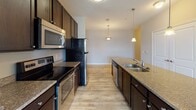 Located at 1533 Ellis Rd in Durham, NC, this single-floor residence offers a well-designed open-concept layout that connects the living and kitchen areas seamlessly. The kitchen is a standout feature, outfitted with rich dark-stained cabinetry, granite countertops, a double-basin stainless steel sink set into a central island, and a full suite of stainless steel appliances including a refrigerator, electric range, and over-the-range microwave. Pendant lighting above the island adds a warm, functional ambiance to the space. The open living area transitions from wood-look flooring in the kitchen and dining zone to plush wall-to-wall carpeting, creating a comfortable and inviting atmosphere. The bedrooms are generously proportioned, each featuring soft carpet flooring, neutral-toned walls, and windows with blinds that allow for natural light and outdoor views. The bathroom includes a soaking tub with a tiled surround and a combination shower, finished in clean white with chrome fixtures. Throughout the space, a consistent neutral color palette, clean lines, and thoughtful finishes contribute to a cohesive and functional living environment.
