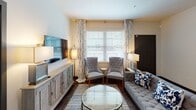 This single-story residence offers a thoughtfully designed layout with a cohesive, contemporary aesthetic throughout. The living room serves as a welcoming gathering space, featuring dark hardwood-style flooring, tufted seating, a media console, and large windows dressed with patterned drapes that invite abundant natural light. The kitchen is equipped with dark espresso cabinetry, stainless steel appliances including a range, over-the-range microwave, and refrigerator, all complemented by light quartz countertops and wood-look flooring. Multiple bedrooms provide comfortable retreats, each finished with plush carpeting, ceiling fans, and windows with outdoor views. The primary bedroom includes a walk-in closet with wire shelving, while a secondary bedroom features a dresser and ample storage. Bathrooms are finished with dark vanity cabinetry, white countertops, and wood-look tile flooring; one includes a glass-enclosed tile shower. A half bath offers a streamlined vanity with a vessel-style sink. An attached single-car garage with an automatic opener and fluorescent lighting completes the residence, adding practical utility to this well-rounded home.