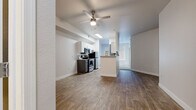 This single-floor unit offers a clean, contemporary layout with a cohesive design throughout. The open-concept living and kitchen area serves as the heart of the space, finished with warm wood-look flooring and crisp white walls. A ceiling fan with light fixture keeps the area comfortable, while a skylight-style overhead fixture brightens the kitchen zone. The kitchen is equipped with stainless steel appliances, including a range, over-the-range microwave, and refrigerator, all complemented by white upper cabinetry and dark lower cabinetry. A peninsula counter provides additional workspace and a natural divide between the kitchen and living area. A hallway connects the main living space to the private areas of the unit. The bedroom is carpeted for added comfort and features a large window dressed with vertical blinds that allow for generous natural light. A mirrored sliding-door closet adds both storage and visual depth to the room, while a ceiling fan provides year-round climate control. The bathroom is efficiently designed with wood-look flooring, a white vanity with modern hardware, a full tub-shower combination with tiled surround, and clean white finishes throughout. The overall aesthetic is neutral and move-in ready.