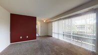 This single-floor residence offers a practical and well-organized layout designed for comfortable living. The expansive living room serves as the heart of the home, featuring plush wall-to-wall carpeting and a striking deep red accent wall that adds a bold visual focal point. A full wall of sliding glass doors lined with vertical blinds fills the space with natural light and provides direct access to an outdoor area, offering views of surrounding greenery. A ceiling light fixture and a subtle beam detail add character to the living area's ceiling.

The kitchen is efficiently designed with rich dark cabinetry, granite-style countertops, a stainless steel sink, and a dishwasher, with tile flooring providing a clean and durable surface. The layout connects easily to the main living and dining areas.

The bedrooms are generously sized, each featuring soft carpeting and windows with vertical blinds that allow for natural light and outdoor views. One bedroom includes a built-in closet with bifold doors, providing ample storage. A second doorway in the bedroom leads to an adjoining space for added convenience.

The bathroom is clean and functional, featuring a tiled tub and shower surround with a decorative mosaic tile accent border, a vanity with a mirror cabinet, and a simple, classic design throughout.