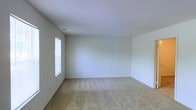 This two-floor space presents a clean and neutral aesthetic throughout, making it an adaptable environment suited to a variety of uses. The interiors are characterized by crisp white walls and smooth ceilings that lend a bright, airy feel to each room. Plush wall-to-wall carpeting in a warm beige tone runs through the living areas, adding comfort underfoot while complementing the light color palette. Natural light filters in through windows, enhancing the open and welcoming ambiance. The layout spans two floors, offering a natural separation of living and private spaces. Each room benefits from a simple, uncluttered design with multiple electrical outlets positioned conveniently along the baseboards. Ceiling vents are integrated seamlessly, suggesting a climate control system for year-round comfort. The overall design is understated and functional, providing a blank canvas that allows for personalization and flexible furnishing arrangements. The combination of soft carpeting, white walls, and natural light creates a calm and neutral atmosphere throughout the entire space.