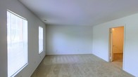 This two-floor space presents a clean and neutral aesthetic throughout, making it an adaptable environment suited to a variety of uses. The interiors are characterized by crisp white walls and smooth ceilings that lend a bright, airy feel to each room. Plush wall-to-wall carpeting in a warm beige tone runs through the living areas, adding comfort underfoot while complementing the light color palette. Natural light filters in through windows, enhancing the open and welcoming ambiance. The layout spans two floors, offering a natural separation of living and private spaces. Each room benefits from a simple, uncluttered design with multiple electrical outlets positioned conveniently along the baseboards. Ceiling vents are integrated seamlessly, suggesting a climate control system for year-round comfort. The overall design is understated and functional, providing a blank canvas that allows for personalization and flexible furnishing arrangements. The combination of soft carpeting, white walls, and natural light creates a calm and neutral atmosphere throughout the entire space.