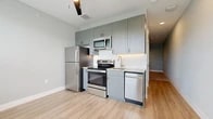 This 1-bedroom, 1-bathroom unit offers a thoughtfully designed single-floor layout that maximizes every inch of its compact footprint. The kitchen serves as a functional centerpiece, outfitted with a full suite of stainless steel appliances including a refrigerator, electric range, built-in microwave, and dishwasher. Sage-toned shaker-style cabinetry extends to the ceiling, providing ample storage, while granite countertops and a tile backsplash add a polished, contemporary aesthetic. Light hardwood-style flooring runs throughout the main living area, contributing to a bright and open feel. The spacious bedroom offers plush carpeting, neutral gray walls, and a generously sized closet with a built-in rod for organization. Dark panel doors throughout the unit provide a striking contrast against the light walls, lending a modern edge to the interior. The bathroom is well-appointed with a granite-topped vanity with undermount sink, a framed mirror, and a full tub-shower combination with large-format tile surround. Brushed nickel fixtures and light wood-style flooring complete the clean, cohesive look. This unit combines smart design with quality finishes to deliver a comfortable and stylish living space.