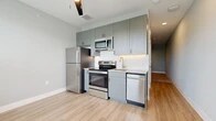 This 1-bedroom, 1-bathroom unit offers a thoughtfully designed single-floor layout that maximizes every inch of its compact footprint. The kitchen serves as a functional centerpiece, outfitted with a full suite of stainless steel appliances including a refrigerator, electric range, built-in microwave, and dishwasher. Sage-toned shaker-style cabinetry extends to the ceiling, providing ample storage, while granite countertops and a tile backsplash add a polished, contemporary aesthetic. Light hardwood-style flooring runs throughout the main living area, contributing to a bright and open feel. The spacious bedroom offers plush carpeting, neutral gray walls, and a generously sized closet with a built-in rod for organization. Dark panel doors throughout the unit provide a striking contrast against the light walls, lending a modern edge to the interior. The bathroom is well-appointed with a granite-topped vanity with undermount sink, a framed mirror, and a full tub-shower combination with large-format tile surround. Brushed nickel fixtures and light wood-style flooring complete the clean, cohesive look. This unit combines smart design with quality finishes to deliver a comfortable and stylish living space.