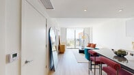 Located in Miami, FL, this thoughtfully designed one-bedroom, one-bathroom residence offers a well-appointed layout that maximizes every square foot across a single floor. The open-concept kitchen is a standout feature, showcasing sleek white upper cabinetry paired with warm wood-toned lower cabinets, light hardwood-style flooring, and a full suite of stainless steel appliances including a refrigerator, range, and over-the-range microwave. A glass-top kitchen island with bold red bar stools provides casual dining and additional workspace, seamlessly connecting the kitchen to the living area. The bedroom is filled with natural light courtesy of large floor-to-ceiling windows that frame panoramic views of the Miami cityscape and surrounding greenery, creating a bright and airy retreat. The room also features light wood flooring and ample storage via a dedicated closet area with built-in shelving. The bathroom is finished with clean, tile flooring and modern fixtures. A private balcony extends the living space outdoors, offering elevated views of the vibrant Miami surroundings, with the building's striking orange and gray contemporary façade visible from outside. Recessed lighting and a clean, neutral color palette throughout contribute to a cohesive, modern ambiance.