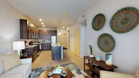 This single-floor residence offers a thoughtfully designed open-concept layout that seamlessly connects the kitchen, dining, and living areas. The kitchen is a standout feature, showcasing rich dark-stained cabinetry that extends to the ceiling for ample storage, granite countertops, and a full suite of stainless steel appliances including a gas range, microwave, and refrigerator. A peninsula island with seating provides additional prep space and a casual dining option, illuminated by pendant lighting overhead. Recessed lighting and light hardwood-style flooring extend throughout the main living area, contributing to a bright and welcoming atmosphere. The living room is generously proportioned, featuring large floor-to-ceiling windows with vertical blinds that allow for abundant natural light. The bedroom is a comfortable retreat with plush carpeting, wide windows fitted with horizontal blinds, a ceiling fan, and ample wall space. The bathroom features dark wood cabinetry, a white countertop vanity, a framed mirror with bright overhead lighting, and a combination tub and shower. Neutral tones and clean lines are carried throughout, creating a cohesive and contemporary aesthetic across every room.