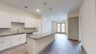 This well-appointed single-floor residence showcases a clean, modern design with thoughtful finishes throughout. The open-concept kitchen is a standout feature, outfitted with crisp white shaker cabinetry, granite countertops, a marble-style tile backsplash, and a full suite of stainless steel appliances including a refrigerator, range, microwave, and dishwasher. A generously sized kitchen island with a matching granite surface provides additional prep space and serves as a natural gathering point. Pendant lighting above the island adds a contemporary touch.

The kitchen flows seamlessly into the living area, which is bathed in natural light from a set of glass French doors that open to an outdoor balcony. A ceiling fan overhead adds comfort and airflow to the space. Durable wood-look flooring runs throughout the main living areas, lending a warm and cohesive aesthetic.

The bedroom is carpeted for comfort and features a large window that invites natural light. It connects directly to a well-designed bathroom, complete with a granite-topped vanity, a glass-enclosed shower, wood-look flooring, and direct access to a spacious walk-in closet with built-in shelving. The overall palette of neutral tones and modern hardware creates a clean, inviting ambiance throughout the residence.