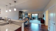 This single-floor residence offers a thoughtfully designed open-concept layout that seamlessly connects the kitchen, dining, and living areas. The kitchen is outfitted with stainless steel appliances, including a refrigerator, range, and microwave, complemented by rich dark wood cabinetry and granite countertops that extend to a breakfast bar. Hardwood flooring flows throughout the main living areas, adding warmth and continuity to the space.

The living area is bright and inviting, featuring a sliding glass door that opens to a private balcony, allowing natural light to fill the room. A dedicated dining space sits adjacent to the living room, providing a defined area for meals and entertaining.

The residence includes multiple bedrooms, each finished with plush carpeting and fitted with ceiling light fixtures. One bedroom benefits from direct balcony access via a glass door, while another features a bay-style window with layered curtains. Both bathrooms are finished with light tile flooring and dark wood vanities with granite countertops; one includes a walk-in shower, and the other features a shower-tub combination.