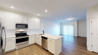 Located at 1500-1514 S Missouri Ave in Morton, Illinois, this single-floor unit offers a clean, modern design with thoughtful finishes throughout. The open-concept layout seamlessly connects the kitchen and living area, creating a bright and functional shared space. The kitchen is well-appointed with white shaker-style cabinetry, white countertops, a peninsula with an undermount sink and matte black faucet, and a full suite of stainless steel appliances including a range, over-the-range microwave, dishwasher, and French door refrigerator with ice and water dispenser. A classic white subway tile backsplash adds a polished touch. The living area features warm wood-look luxury vinyl plank flooring and a sliding glass door with vertical blinds that invites natural light. Bedrooms are finished with plush carpet, ceiling fans, and multiple windows offering ample brightness. The bathroom maintains a crisp, all-white aesthetic with tile flooring, a tub/shower combination, white vanity with quartz-style countertop, and striking matte black hardware and fixtures throughout. Recessed lighting and consistent white walls give the entire unit a clean, contemporary feel.