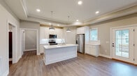 Located at 5833 Evans Farm Dr. in Lewis Center, Ohio, this single-floor home offers a thoughtfully designed open-concept layout with modern finishes throughout. The entryway leads down a clean, well-lit hallway with recessed lighting and durable hardwood-style flooring, providing a welcoming introduction to the home.

The kitchen is a standout feature, showcasing white shaker-style cabinetry, stainless steel appliances including a range, microwave, and refrigerator, and a large center island with a double sink and light countertops. Dual industrial-style pendant lights hang above the island, adding a contemporary touch. The kitchen flows seamlessly into the open living area, which is defined by an elegant tray ceiling, recessed lighting, a ceiling fan, and French doors that allow natural light to pour in while providing views of the outdoors.

A full bathroom features a tub-shower combination with white tile surround, a white vanity, and wood-look flooring. The home also includes a dedicated laundry area equipped with a full-size washer and dryer, as well as a walk-in closet with wire shelving for generous storage. The attached two-car garage offers additional utility space with an automatic opener. Neutral tones and clean architectural lines create a cohesive, move-in-ready atmosphere throughout.