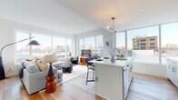 This thoughtfully designed single-floor residence combines contemporary style with urban convenience. The open-concept living, dining, and kitchen area is the heart of the home, bathed in abundant natural light streaming through expansive floor-to-ceiling windows that frame impressive city skyline views. Light hardwood flooring flows throughout, adding warmth to the bright, neutral palette.

The kitchen is outfitted with white cabinetry, a classic subway tile backsplash, stainless steel appliances — including a range, microwave, and refrigerator — and a sleek island with white countertops that doubles as a dining and prep space. A dedicated in-unit laundry area with stacked washer and dryer adds everyday convenience.

The living room offers generous space for relaxation, anchored by large picture windows overlooking the urban landscape. Both bedrooms are well-proportioned, featuring hardwood floors and large windows that invite natural light and cityscape views. The primary bathroom includes a glass-enclosed shower, a wide vanity with integrated sink, and large-format tile flooring. A second full bathroom features a tiled soaking tub and a streamlined vanity. Clean lines, modern fixtures, and a cohesive design aesthetic create a polished, comfortable living environment throughout.