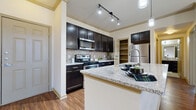 This single-floor residence offers a well-designed open-concept layout that seamlessly connects the kitchen and living areas. The kitchen is a standout feature, outfitted with dark espresso cabinetry, granite countertops, a tile mosaic backsplash, and a full suite of stainless steel appliances including a range, microwave, dishwasher, and refrigerator. Track lighting illuminates the prep areas, while pendant lights hang above the central island, which also features an integrated sink — ideal for both cooking and casual dining. Crown molding adds a refined architectural detail throughout the main living spaces.

The open living area extends naturally from the kitchen, benefiting from natural light through window blinds and a ceiling fan that enhances comfort and airflow. Wood-look flooring runs throughout the main areas, contributing to a warm, cohesive aesthetic.

The bedroom is a quiet retreat, carpeted for comfort, with direct access to a generously sized walk-in closet equipped with multiple shelving tiers and hanging rods for ample storage. The bathroom features large-format neutral tile flooring, a full soaking tub with tiled surround, a dark vanity with granite countertop, and chrome fixtures.

A dedicated in-unit laundry room houses a full-size washer and dryer alongside additional shelving, completing this functional and well-appointed living space.