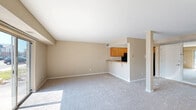This one-bedroom, one-bathroom unit in Grand Blanc, Michigan offers a well-organized, single-floor layout designed for comfortable everyday living. The combined living and dining area is generously proportioned, featuring neutral-toned carpet, warm beige walls, and a distinctive structural column that adds architectural character to the open space. A full-width sliding glass door floods the living area with natural light and provides direct outdoor access, offering views of the surrounding community and mature trees. The kitchen is thoughtfully designed with warm wood cabinetry, granite-look countertops, a breakfast bar pass-through, and black appliances including a range and refrigerator. A hallway connects the main living area to the private bedroom, which is carpeted and bright, with a large window fitted with vertical blinds that allow ample natural light. The bedroom includes a dedicated closet with built-in shelving, and the unit offers a total of three closets for additional storage. The full bathroom features tile flooring, a white vanity with a large mirror, and a tub-shower combination. The clean, neutral palette throughout the unit creates a bright and move-in-ready atmosphere.