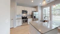 This well-appointed single-floor residence showcases a thoughtfully designed layout that balances functionality with modern aesthetics. The kitchen serves as a central highlight, featuring crisp white shaker-style cabinetry, sleek gray quartz countertops, and a classic white subway tile backsplash. A full suite of stainless steel appliances — including a side-by-side refrigerator with ice and water dispenser, an electric range, and an over-the-range microwave — complement the space. A kitchen island with an integrated sink and pendant lighting adds both workspace and visual interest, while light hardwood-style flooring runs throughout the main areas, lending warmth and continuity. The living area is bright and open, benefiting from multiple windows dressed with horizontal blinds that invite natural light and views of the surrounding neighborhood. A ceiling fan provides comfort and adds a casual, inviting touch. The bedroom area is carpeted for comfort and includes a built-in desk nook as well as a spacious reach-in closet equipped with wire shelving and hanging rods, offering practical storage. Neutral gray wall tones throughout create a clean, modern backdrop that suits a variety of décor styles. The overall ambiance is fresh, bright, and move-in ready.