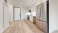 Located in Ottawa's Kanata neighbourhood at Campeau Drive, this one-bedroom, one-bathroom unit offers a well-designed layout across a single floor. Light-toned hardwood flooring runs throughout the space, creating a cohesive and clean aesthetic.

The kitchen is a standout feature, equipped with full stainless steel appliances including an LG range, over-the-range microwave, dishwasher, and a French door refrigerator. White shaker-style cabinetry with gold-toned hardware pairs with a marble-look quartz backsplash and countertops, delivering a modern and polished finish.

The bedroom is a comfortable, well-proportioned room featuring large floor-to-ceiling windows that invite abundant natural light and offer views of the surrounding landscape. The crisp white walls and light flooring enhance the bright, airy atmosphere.

The bathroom is finished to a high standard, showcasing full-height marble-patterned wall tiles enclosing a walk-in glass shower with a built-in bench, handheld showerhead, and a frosted window for natural light. Large-format floor tiles complete the refined look.

Two hallways provide practical circulation through the unit. The overall design is contemporary and cohesive, with a neutral palette, quality finishes, and thoughtful details throughout.
