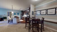 This single-floor residence offers a thoughtfully designed open-concept layout that seamlessly connects the kitchen, dining, and living areas. The kitchen is a standout feature, showcasing rich dark-walnut cabinetry extending to the ceiling, granite countertops, a classic white subway tile backsplash, stainless steel appliances including a refrigerator, range, microwave, and dishwasher, and hardwood-style flooring. A kitchen island provides additional counter space and casual seating. The adjacent dining area accommodates a full dining set, while track lighting overhead adds a modern touch.

The living room is generously proportioned with plush carpeting, soothing blue-gray walls, and large windows fitted with plantation shutters that allow ample natural light. The space comfortably houses a seating arrangement and media console.

The bedrooms continue the warm, neutral palette, each featuring carpeted floors, windows with blinds and curtain panels, and ample room for full bedroom furnishings. The bathrooms are finished with dark cabinetry, granite countertops, large mirrors, hardwood-style flooring, and built-in shelving for storage. Overall, the residence presents a cohesive, contemporary aesthetic with a comfortable and functional atmosphere throughout.