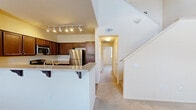 This two-story residence is thoughtfully laid out across two levels, providing a comfortable and functional living environment. The main floor is the more spacious of the two and centers around an open-concept kitchen and dining area. The kitchen is equipped with rich dark wood cabinetry, stainless steel appliances including a refrigerator and built-in microwave, and a granite-topped breakfast bar with decorative corbels — ideal for casual dining or entertaining. Track lighting illuminates the space, and soft carpeting extends throughout the living areas. A staircase with clean white railings connects the main level to the upper floor, where both bedrooms are located. The generously sized primary bedroom features plush carpeting, a ceiling fan, and a walk-in closet. The second bedroom is equally comfortable, also carpeted, and includes a ceiling fan and a window that invites natural light. Three bathrooms serve the home, including one with a tub-shower combination, wood-look flooring, and a granite-topped vanity. A dedicated laundry room with a full-size side-by-side washer and dryer adds everyday convenience. The overall aesthetic is clean and neutral, with warm tones and practical finishes throughout.