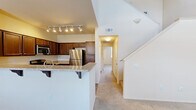 This two-story residence is thoughtfully laid out across two levels, providing a comfortable and functional living environment. The main floor is the more spacious of the two and centers around an open-concept kitchen and dining area. The kitchen is equipped with rich dark wood cabinetry, stainless steel appliances including a refrigerator and built-in microwave, and a granite-topped breakfast bar with decorative corbels — ideal for casual dining or entertaining. Track lighting illuminates the space, and soft carpeting extends throughout the living areas. A staircase with clean white railings connects the main level to the upper floor, where both bedrooms are located. The generously sized primary bedroom features plush carpeting, a ceiling fan, and a walk-in closet. The second bedroom is equally comfortable, also carpeted, and includes a ceiling fan and a window that invites natural light. Three bathrooms serve the home, including one with a tub-shower combination, wood-look flooring, and a granite-topped vanity. A dedicated laundry room with a full-size side-by-side washer and dryer adds everyday convenience. The overall aesthetic is clean and neutral, with warm tones and practical finishes throughout.