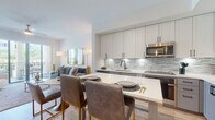 Located at 5400 Broken Sound Blvd NW in Boca Raton, Florida, this single-floor residence offers a thoughtfully designed open-concept layout with contemporary finishes and a cohesive, modern aesthetic throughout. Light wood-tone flooring extends across the main living areas, complementing the neutral color palette and creating a bright, welcoming atmosphere.

The kitchen is a standout feature, equipped with stainless steel appliances including a full-size refrigerator, microwave, and built-in oven. Two-tone cabinetry in white and soft gray is paired with white quartz countertops and a textured tile backsplash. A peninsula with bar seating bridges the kitchen to the dining and living areas, facilitating an easy flow for entertaining.

The living room opens directly onto a private balcony through floor-to-ceiling sliding glass doors, offering views of the surrounding landscaping and pool area. A ceiling fan enhances comfort in this sun-filled space. Bedrooms are serene and well-proportioned, each featuring large windows with views of palm trees and ample natural light.

The bathroom includes a tub-shower combination with marble-style surround tiling and matte black fixtures, adding a refined touch. Track lighting, clean architectural lines, and quality finishes throughout contribute to the polished, move-in-ready character of this Boca Raton residence.