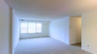 This single-floor space offers a clean, functional layout spread across several well-defined rooms. The floor plan, as viewed from above, reveals a thoughtfully arranged interior with distinct living, sleeping, and utility areas connected by a logical flow of corridors and open transitions.

The main living area is notably spacious, featuring soft wall-to-wall carpeting in a neutral tone that adds warmth underfoot. Large windows span a prominent wall, inviting an abundance of natural light that brightens the entire room and creates an airy, open atmosphere. The white walls and smooth ceilings further enhance the sense of openness, giving the space a clean and versatile canvas.

Additional rooms visible in the floor plan reflect a similar design philosophy — neutral finishes, white walls, and consistent flooring materials that tie the interior together cohesively. The layout suggests a practical separation of spaces while maintaining an overall sense of flow and connectivity throughout.

The space is currently vacant, making it easy to appreciate its architectural structure and the potential it holds. The combination of generous natural light, open proportions, and a straightforward layout makes this a highly adaptable space suitable for a variety of uses.