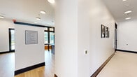 Located at Shoals Point Trail in Madison, Alabama, this thoughtfully designed single-floor amenity space offers a refined blend of modern aesthetics and functional layout. The interior is unified by light wood-look flooring, crisp white walls, and bold dark trim and window framing that create a striking contemporary contrast throughout.

The dining room serves as a welcoming gathering area, centered around a solid wood table with sage green upholstered chairs. A built-in wet bar with dark navy cabinetry, gold hardware, and an open shelf adds convenience, while a wall-mounted TV and decorative botanical wallpaper accent bring warmth and character to the space. Large black-framed windows flood the room with natural light and offer views of the surrounding neighborhood.

The living room, accessible through sleek glass-paned doors, functions as a versatile conference or lounge area. It features a bold geometric area rug, a round table with modern seating, a wall-mounted display, and a stylish pendant light. Expansive windows provide ample daylight and outdoor views.

The hallway connects the spaces seamlessly and includes a well-organized mail and package center, featuring banks of numbered mailboxes and smart parcel lockers. Recessed and pendant lighting illuminate the corridor, which is further enhanced by framed artwork and clean architectural lines throughout.
