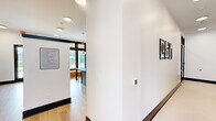 Located at Shoals Point Trail in Madison, Alabama, this thoughtfully designed single-floor amenity space offers a refined blend of modern aesthetics and functional layout. The interior is unified by light wood-look flooring, crisp white walls, and bold dark trim and window framing that create a striking contemporary contrast throughout.

The dining room serves as a welcoming gathering area, centered around a solid wood table with sage green upholstered chairs. A built-in wet bar with dark navy cabinetry, gold hardware, and an open shelf adds convenience, while a wall-mounted TV and decorative botanical wallpaper accent bring warmth and character to the space. Large black-framed windows flood the room with natural light and offer views of the surrounding neighborhood.

The living room, accessible through sleek glass-paned doors, functions as a versatile conference or lounge area. It features a bold geometric area rug, a round table with modern seating, a wall-mounted display, and a stylish pendant light. Expansive windows provide ample daylight and outdoor views.

The hallway connects the spaces seamlessly and includes a well-organized mail and package center, featuring banks of numbered mailboxes and smart parcel lockers. Recessed and pendant lighting illuminate the corridor, which is further enhanced by framed artwork and clean architectural lines throughout.