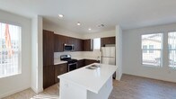This single-floor space showcases a thoughtfully designed kitchen that serves as the heart of the layout. The kitchen features rich, dark espresso-toned cabinetry that lines the walls in an L-shaped configuration, providing generous storage and a sleek, contemporary aesthetic. The cabinetry is complemented by clean white countertops that extend throughout, creating a striking contrast.

A central island anchors the space, finished in bright white quartz with a double undermount sink, offering additional workspace and a natural gathering point. Stainless steel appliances, including a gas range, over-the-range microwave, and a full-size refrigerator, add a professional quality to the kitchen.

The flooring consists of light-toned wood-look planks that run throughout, contributing warmth and continuity to the space. Recessed lighting in the white ceiling ensures even, practical illumination, while a window above the counter allows natural light to filter in. The overall design is clean and modern, balancing functional efficiency with a polished, contemporary finish.