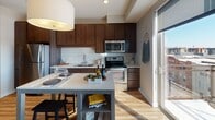 Located at 1300 W Lake St in the vibrant Uptown neighborhood of Minneapolis, this contemporary single-floor residence offers a well-designed open-concept layout finished with light hardwood flooring throughout. The kitchen is a standout feature, equipped with rich dark wood cabinetry extending to the ceiling, a classic white subway tile backsplash, stainless steel appliances including a refrigerator, range, microwave, and dishwasher, and a light-toned countertop that provides ample prep space. A dining area with a central table sits adjacent to the kitchen, ideal for everyday meals or entertaining. The living area is bright and airy, benefiting from floor-to-ceiling sliding glass doors that open to an outdoor balcony, flooding the space with natural light and offering open city views. A stylish barn-style sliding door connects the hallway to the bedroom, which features carpeted flooring and a cozy, well-appointed layout. The bathroom is finished with large-format dark tile flooring, a wall-tiled soaking tub and shower combination, a floating wood-accented vanity, and recessed lighting, creating a clean and modern aesthetic. The overall design balances urban contemporary style with functional, comfortable living.