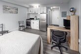 Located on the 8th floor at 186 King Street in downtown London, Ontario, this efficiently designed unit offers 1 bedroom and 2 bathrooms within a compact, well-organized floor plan. The main living area flows seamlessly from a small entry hallway into the bedroom, which serves as the central living space. Large floor-to-ceiling windows dressed with rich burgundy curtains flood the room with natural light and frame elevated city views, creating an airy atmosphere despite the unit's modest footprint. Hardwood-style laminate flooring runs throughout, lending a clean, contemporary feel. The bedroom comfortably accommodates a full-sized bed, a dedicated workspace with a desk and ergonomic chair, and additional shelving for storage. A stainless steel refrigerator and overhead cabinetry indicate an integrated kitchen area within the open layout. The unit includes two bathrooms: a half-bath featuring tile flooring, a white vanity with an undermount sink, and clean white walls, and a second bathroom equipped with a full tub-shower combo finished with classic white subway-style tiling. The overall design is bright, neutral, and practical, making this an informative and functional urban living space well-suited for individuals or students in the heart of London's downtown core.