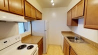 This single-floor unit offers a practical and straightforward layout designed for comfortable everyday living. The galley-style kitchen is efficiently arranged with warm honey-toned wood cabinetry lining both walls, providing generous upper and lower storage. Granite-look laminate countertops run along each side, complemented by a stainless steel sink, a white electric coil-burner range, a full-size refrigerator, and a dishwasher. Track lighting overhead illuminates the workspace, and a window on one end brings in natural light.

The living area features neutral carpet, a ceiling fan with light fixture, and a large sliding glass door dressed with vertical blinds, allowing ample natural light. A wall-mounted air conditioning unit and baseboard heating provide year-round climate control. A small niche in the dividing wall adds a subtle architectural detail.

The bedrooms are carpeted and bright, with one featuring a window with blinds and baseboard heating, and another offering a reach-in closet with built-in wire shelving for organized storage.

The bathroom presents classic mosaic tile flooring in a cream and brown pattern, a white vanity, toilet, and a full tub-shower combination, creating a clean and timeless finish throughout.