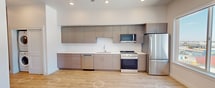 This 390-square-foot studio apartment at 455 W 500 S, Salt Lake City, UT 84101 offers a well-designed single-floor layout with modern finishes throughout. The open living area features light wood-tone luxury vinyl flooring, neutral warm-beige walls, and a ceiling fan, creating a clean and functional space. A large picture window frames striking views of the surrounding Salt Lake City skyline and Wasatch mountain foothills, filling the room with natural light.

The kitchen is outfitted with flat-front taupe cabinetry — both upper and lower — paired with crisp white countertops and a full suite of stainless steel appliances, including a gas range, over-the-range microwave, dishwasher, and a full-size refrigerator. The kitchen's contemporary design maximizes storage and counter space efficiently within the studio layout.

The bathroom continues the modern aesthetic with matching wood-tone cabinetry, a white vanity countertop, a large mirror, and light wood-tone flooring. The space includes a bathtub with a shower curtain rod and grab bar, reflecting an accessible and practical design. Overall, this studio presents a compact yet thoughtfully appointed living space in a contemporary residential setting.