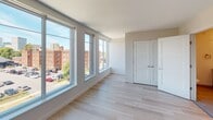 Located at 242–244 Alexander St in Rochester's vibrant East End neighborhood, this single-floor unit showcases a clean, contemporary design with consistent light hardwood flooring and a neutral color palette throughout. The open-concept kitchen is well-appointed with dark walnut-toned shaker cabinetry, light countertops, and a full suite of stainless steel appliances including a range, built-in microwave, refrigerator, and dishwasher. A peninsula with pendant lighting separates the kitchen from the living area, creating a functional and stylish transition between spaces. The living area is generously sized and bright, benefiting from recessed lighting and an airy, open feel. Bedrooms feature large windows that invite substantial natural light and offer views of the surrounding Rochester streetscape and greenery, with one room showcasing a wall of oversized windows providing panoramic city views. Sliding panel closets provide streamlined storage. The bathroom is finished with tile flooring, a framed vanity mirror, walnut-toned cabinetry, and a light countertop, maintaining the cohesive modern aesthetic found throughout the unit.