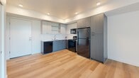 Located in Wilsonville, Oregon, this well-designed one-bedroom, one-bathroom unit offers a thoughtful layout across a single floor. Light wood-tone flooring runs throughout the entire space, creating a cohesive and clean aesthetic. The open-concept kitchen and living area form the heart of the unit, where the kitchen features two-tone cabinetry in gray and white, white quartz countertops, a stainless undermount sink, and a full suite of black appliances including a refrigerator, range, microwave, and dishwasher. Recessed lighting illuminates the kitchen, while large floor-to-ceiling windows in the living area invite abundant natural light and offer views of the surrounding landscape. A ceiling fan adds both function and style to the living space. The bedroom is a comfortable, well-proportioned room with a ceiling fan, a window with an in-unit climate control unit, and direct access to a walk-in closet equipped with wire shelving. A second closet provides additional storage. The bathroom features light wood flooring, a full tub-shower combination, a wood-toned vanity with white countertop, and a backlit mirror. The unit presents a modern, clean finish throughout, making it a practical and stylish living space.