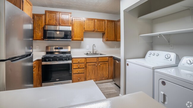 Cocina con electrodomésticos de acero inoxidable, cálidos gabinetes de madera y lavadora y secadora en la unidad para su comodidad. - Legacy at West Cobb