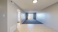 Located at 7000 W Central Ave in Wichita, Kansas, this two-bedroom, one-bathroom unit offers a practical and efficiently designed single-floor layout. The living area features a combination of light tile flooring and plush carpet, with cool blue-gray walls and vertical blinds covering a sliding glass door that allows natural light to fill the room. The spacious primary bedroom is notably generous in size, finished with warm tan carpet, neutral gray walls, and a built-in closet with open shelving for ample storage. The second bedroom is similarly carpeted and bathed in natural light from a window with blinds, offering a comfortable and quiet retreat. A second closet provides additional storage throughout the unit. The full bathroom is cleanly appointed with beige tile flooring, a full-size soaking tub with a tiled surround, and brushed nickel fixtures. A hallway connects the rooms, contributing to a logical and easy-to-navigate floor plan. Textured ceilings are consistent throughout, and flush-mount lighting fixtures provide overhead illumination in key areas. The unit's neutral color palette and functional design make it a versatile and move-in-ready space.