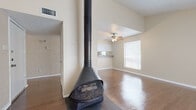This single-story residence offers a well-designed layout with a variety of notable architectural and functional details throughout. The living area immediately draws attention with its dramatic suspended, cone-shaped fireplace — a striking focal point that anchors the room. Vaulted ceilings add a sense of openness and volume, while warm hardwood-style flooring extends across the main living spaces. A ceiling fan overhead and multiple windows allow for natural light and comfortable airflow.

The kitchen is outfitted with white cabinetry, stone-toned countertops, and stainless steel appliances including a refrigerator and dishwasher. A dedicated walk-in pantry provides generous storage, and the galley-style layout makes efficient use of the available space.

The bedrooms feature plush carpet flooring and vaulted ceilings, each equipped with a ceiling fan and windows that admit natural light. Closet space is well-considered, with at least one bedroom offering a spacious walk-in closet complete with built-in shelving on both sides.

The bathroom includes a vanity with white cabinetry, stone-toned countertops, and a bathtub/shower combination. Throughout the residence, textured walls, clean white trim, and neutral tones create a cohesive, understated aesthetic that is both practical and inviting.