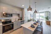 Located in Fort Myers, FL, this well-appointed 2-bedroom, 2-bathroom residence offers a thoughtfully designed single-floor layout that balances comfort and modern style. The open-concept living area seamlessly connects the kitchen, dining, and living spaces, all bathed in natural light from large sliding glass doors leading to a private balcony with pleasant outdoor views. The kitchen is a standout feature, boasting a generous quartz-topped island with bar seating, sleek gray cabinetry, stainless steel appliances, and stylish pendant lighting overhead. Light wood-tone flooring flows throughout the main living areas, enhancing the bright, airy ambiance. The combined dining and living room provides a comfortable gathering space, while a ceiling fan adds to the breezy Florida feel. Both bedrooms are carpeted and well-sized, with the primary bedroom offering ample natural light and a spacious walk-in closet with built-in shelving. The two bathrooms are clean and modern — one featuring a tub/shower combination and the other a glass-enclosed shower. Additional highlights include a laundry area, utility room, hallway, and five closets throughout, ensuring exceptional storage. This residence offers a polished, contemporary lifestyle in a practical and efficient floor plan.