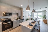 Located in Fort Myers, FL, this well-appointed 2-bedroom, 2-bathroom residence offers a thoughtfully designed single-floor layout that balances comfort and modern style. The open-concept living area seamlessly connects the kitchen, dining, and living spaces, all bathed in natural light from large sliding glass doors leading to a private balcony with pleasant outdoor views. The kitchen is a standout feature, boasting a generous quartz-topped island with bar seating, sleek gray cabinetry, stainless steel appliances, and stylish pendant lighting overhead. Light wood-tone flooring flows throughout the main living areas, enhancing the bright, airy ambiance. The combined dining and living room provides a comfortable gathering space, while a ceiling fan adds to the breezy Florida feel. Both bedrooms are carpeted and well-sized, with the primary bedroom offering ample natural light and a spacious walk-in closet with built-in shelving. The two bathrooms are clean and modern — one featuring a tub/shower combination and the other a glass-enclosed shower. Additional highlights include a laundry area, utility room, hallway, and five closets throughout, ensuring exceptional storage. This residence offers a polished, contemporary lifestyle in a practical and efficient floor plan.