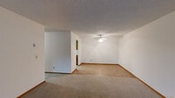 This single-floor residential unit offers a well-organized layout with clearly defined living spaces connected by a carpeted hallway. The hallway features a textured ceiling, flush lighting, and warm wood-toned doors with matching trim, lending a cohesive aesthetic throughout.

The galley-style kitchen is efficiently designed with rich wood cabinetry, light laminate flooring, and stainless steel appliances including a refrigerator, range, and dishwasher. A double basin sink sits beneath under-cabinet lighting, and a skylight above brightens the space. The kitchen opens directly into the main living area, which features a ceiling fan, neutral walls, and a smooth transition between carpet and laminate flooring.

The spacious living room is bright and open, with a large sliding glass door framed by vertical blinds that allows natural light to pour in and provides outdoor views of surrounding greenery. Baseboard heating runs along the perimeter walls.

The bedrooms are carpeted and well-sized, each featuring windows with vertical blinds and wall-mounted utility panels. At least one bedroom includes a generous reach-in closet with a full-width shelf and hanging rod behind warm wood bifold doors. The textured ceilings and neutral color palette throughout create a clean, functional living environment.
