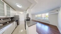 Located at 7 Elizabeth St N in Mississauga's charming Port Credit neighbourhood, this one-bedroom, one-bathroom unit offers a well-designed layout across a single floor. Rich hardwood flooring flows throughout the living room and bedroom, creating a warm and cohesive aesthetic, while large windows flood both spaces with natural light and frame views of the surrounding urban greenery and cityscape.

The galley-style kitchen is thoughtfully appointed with white cabinetry featuring frosted glass upper panels, dark grey countertops, a tile backsplash with decorative accents, stainless steel appliances, and light ceramic tile flooring. A half-wall with a breakfast bar connects the kitchen to the open living area, which is spacious enough for comfortable furnishing and benefits from a wall-mounted air conditioning unit.

The bedroom is a comfortable retreat, featuring hardwood floors, a built-in closet, and a large window that brings in ample natural light. The bathroom is finished with floor-to-ceiling neutral tile surrounding a full soaker tub and shower combination, complemented by clean white fixtures and chrome hardware. The unit presents a clean, move-in ready interior with a bright and functional design throughout.