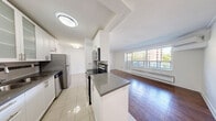Located at 7 Elizabeth St N in Mississauga's charming Port Credit neighbourhood, this one-bedroom, one-bathroom unit offers a well-designed layout across a single floor. Rich hardwood flooring flows throughout the living room and bedroom, creating a warm and cohesive aesthetic, while large windows flood both spaces with natural light and frame views of the surrounding urban greenery and cityscape.

The galley-style kitchen is thoughtfully appointed with white cabinetry featuring frosted glass upper panels, dark grey countertops, a tile backsplash with decorative accents, stainless steel appliances, and light ceramic tile flooring. A half-wall with a breakfast bar connects the kitchen to the open living area, which is spacious enough for comfortable furnishing and benefits from a wall-mounted air conditioning unit.

The bedroom is a comfortable retreat, featuring hardwood floors, a built-in closet, and a large window that brings in ample natural light. The bathroom is finished with floor-to-ceiling neutral tile surrounding a full soaker tub and shower combination, complemented by clean white fixtures and chrome hardware. The unit presents a clean, move-in ready interior with a bright and functional design throughout.