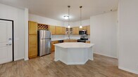 Located at 808 Berry St in Saint Paul, Minnesota, this two-bedroom, two-bathroom residence offers a well-designed single-floor layout with a clean, neutral aesthetic throughout. The open-concept living and kitchen area serves as the heart of the space, where warm hardwood-style flooring extends seamlessly from the kitchen into the living room. A large picture window with vertical blinds allows abundant natural light to fill the living area, creating a bright and airy atmosphere. The kitchen is well-appointed with warm-toned wood cabinetry, stainless steel appliances including a refrigerator, electric range, and over-the-range microwave, as well as a dishwasher. A central island with a white countertop provides additional prep space and is complemented by pendant lighting overhead. Both bathrooms are consistent in design, featuring wood-toned vanities with white countertops, tub-shower combinations, and hardwood-style flooring. The two bedrooms offer a comfortable retreat, with plush carpeting underfoot. The primary bedroom is generously sized and includes a closet, while a secondary bedroom provides flexible use. The overall ambiance is clean, functional, and move-in ready.
