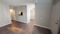 This two-floor residence offers a well-organized layout designed to maximize functionality across its living spaces. The main level features rich, dark wood-style flooring that extends throughout the open living and dining areas, complemented by neutral gray walls and clean white baseboards. A pass-through window connects the living area to the galley-style kitchen, which is equipped with white cabinetry, dual-basin sink, laminate countertops, black appliances including a refrigerator and electric range, and track lighting overhead. A dedicated door off the kitchen provides additional storage or utility access.

The upper level hosts the bedroom, where vaulted ceilings add a sense of openness and a window allows natural light to fill the space. Soft carpeting carries through the bedroom and into a spacious walk-in closet outfitted with built-in shelving units and hanging rods, offering ample organization options. The full bathroom features wood-style flooring, a vanity with granite-style countertops, white cabinetry, and a tub-shower combination with tiled surround. Ceiling fans and HVAC vents are present throughout, contributing to year-round comfort.
