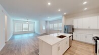 Located at 17003 Telge Road in Cypress, TX, this single-story home offers a well-designed open-concept layout with four bedrooms, two bathrooms, and a dedicated laundry room. Light wood-look flooring flows seamlessly throughout, complementing the home's clean, modern aesthetic and neutral color palette.

The heart of the home is a bright kitchen and living area combination, where a large central island with a sink and white quartz countertops serves as the focal point. White shaker cabinetry reaches to the upper walls, and stainless steel appliances — including a gas range, microwave, and French door refrigerator — complete the space. Recessed lighting and multiple windows with blinds fill the area with natural light, while a ceiling fan enhances comfort in the adjoining living room.

The bedrooms are well-proportioned, each featuring light wood flooring, neutral walls, and windows that bring in natural light. The primary bedroom is a comfortable retreat with an en-suite bathroom offering a dual-sink vanity with white cabinetry, a large mirror, and access to a walk-in closet with built-in shelving and hanging rods. The laundry room includes a full-size washer and dryer with overhead shelving. The attached garage provides ample parking and storage, and features a pull-down attic ladder for additional overhead storage.