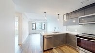 This contemporary 550 square foot apartment at 345 Harrison showcases a thoughtful design that maximizes space and functionality. The open-concept layout seamlessly integrates the living room, dining area, and kitchen, creating a spacious feel. The primary bedroom, measuring 140 square feet, provides ample space for relaxation.

The kitchen is a highlight, boasting sleek stainless steel appliances, including a large refrigerator, built-in microwave, and modern oven. Stylish gray cabinetry complements the hexagonal tile backsplash, while a sizeable island with a quartz countertop offers additional workspace and casual dining.

Large windows throughout flood the space with natural light and frame urban views. The bathroom features a modern vanity with wooden cabinetry, a white countertop, and gray tile flooring. Hardwood floors in a warm, varied tone run throughout the main living areas, adding warmth and sophistication.

The apartment's neutral color palette, clean lines, and minimalist design create a canvas for personal style. Built-in closets and smart storage solutions help maximize the compact floor plan. This well-appointed urban dwelling combines style and efficiency in a prime location.