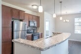 This single-story residence offers a thoughtfully designed layout encompassing two bedrooms, two bathrooms, a combined dining room, kitchen, and living area, two closets, and a dedicated laundry room. The open-concept kitchen is a standout feature, showcasing warm wood cabinetry, granite countertops, stainless steel appliances, a mosaic tile backsplash, and a peninsula with an undermount sink illuminated by sleek pendant lighting — all set atop durable light hardwood flooring that extends through the main living areas. The spacious primary bedroom is generously sized, finished with plush carpet and a ceiling fan, and includes its own bathroom featuring rich wood vanity cabinetry, a wide countertop, and a large mirror with modern overhead lighting. The second bedroom is equally comfortable, also carpeted, and benefits from a ceiling fan and a large window with views of the surrounding community. The living area transitions between hardwood and carpet, with natural light streaming in through sliding glass doors fitted with vertical blinds. A dedicated laundry room houses a full-size washer and dryer. Throughout, neutral warm tones and clean finishes create a bright, cohesive, and move-in-ready atmosphere.
