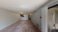 This single-floor residence offers a practical and comfortable layout designed for everyday living. The expansive living room is finished with plush wall-to-wall carpeting, soft gray-toned walls, and a ceiling fan with integrated lighting. A pass-through opening connects the living area to the kitchen, maintaining an open and airy feel throughout the space. The kitchen is well-appointed with rich, dark espresso cabinetry, granite-look countertops, and a full suite of black appliances including an electric range with over-the-range microwave and a full-size refrigerator, all set atop warm hardwood-style flooring. The bedrooms feature the same plush carpeting as the main living area, with neutral gray walls and windows that bring in natural light and views of surrounding greenery. Closet storage is available in the bedroom, adding to the unit's functionality. The bathroom is cleanly finished with a dark-toned vanity cabinet, white countertop, a large mirror with overhead lighting, and a full tub and shower combination clad in classic white tile. Throughout the residence, consistent design elements — including neutral wall tones, white trim, and updated fixtures — contribute to a cohesive and move-in-ready atmosphere.