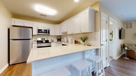 Located at 8900 Alleghany Rd in Corfu, NY, this single-floor, 2-bedroom residence offers a thoughtfully designed layout that maximizes comfort and functionality. The open-concept living and dining area is anchored by warm hardwood-style flooring, with a dining space that flows seamlessly into the living room. The living room is bright and welcoming, featuring large sliding glass doors that invite natural light and provide views of the outdoors. The kitchen is a standout feature, showcasing white shaker-style cabinetry, a marble-inspired tile backsplash, light quartz countertops, and a full suite of stainless steel appliances including a refrigerator, range, microwave, and dishwasher. A peninsula with bar seating adds both functionality and casual dining space. The spacious primary bedroom is carpeted and features a large sliding closet and convenient access to an in-unit stacked washer and dryer. A second bedroom, also carpeted and well-lit by a window, includes a sliding closet and provides flexible use as a guest room or office. Warm neutral tones throughout create a cohesive and calming ambiance across the entire residence.